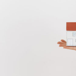 close-up-of-human-hand-holding-mini-house-model-on-white-backdrop